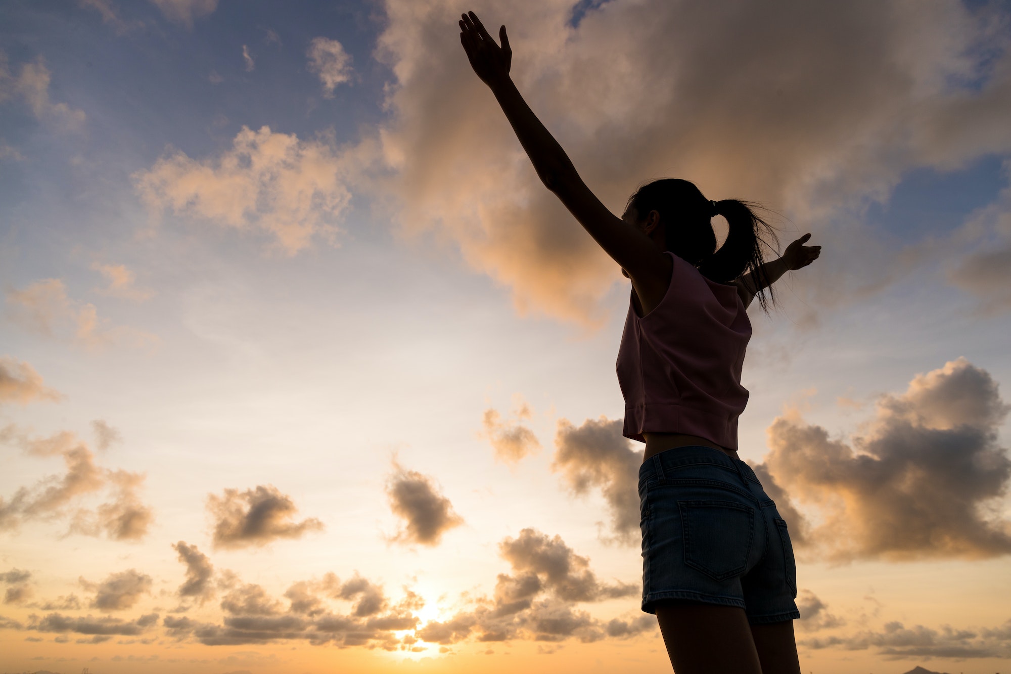 Silhouette woman hands up against sunset time